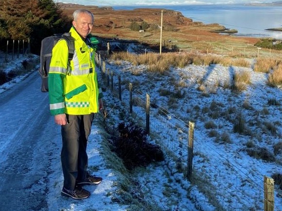 Skye volunteer Steve Brealey dressed in high vis jacket standing on a snow covered road.