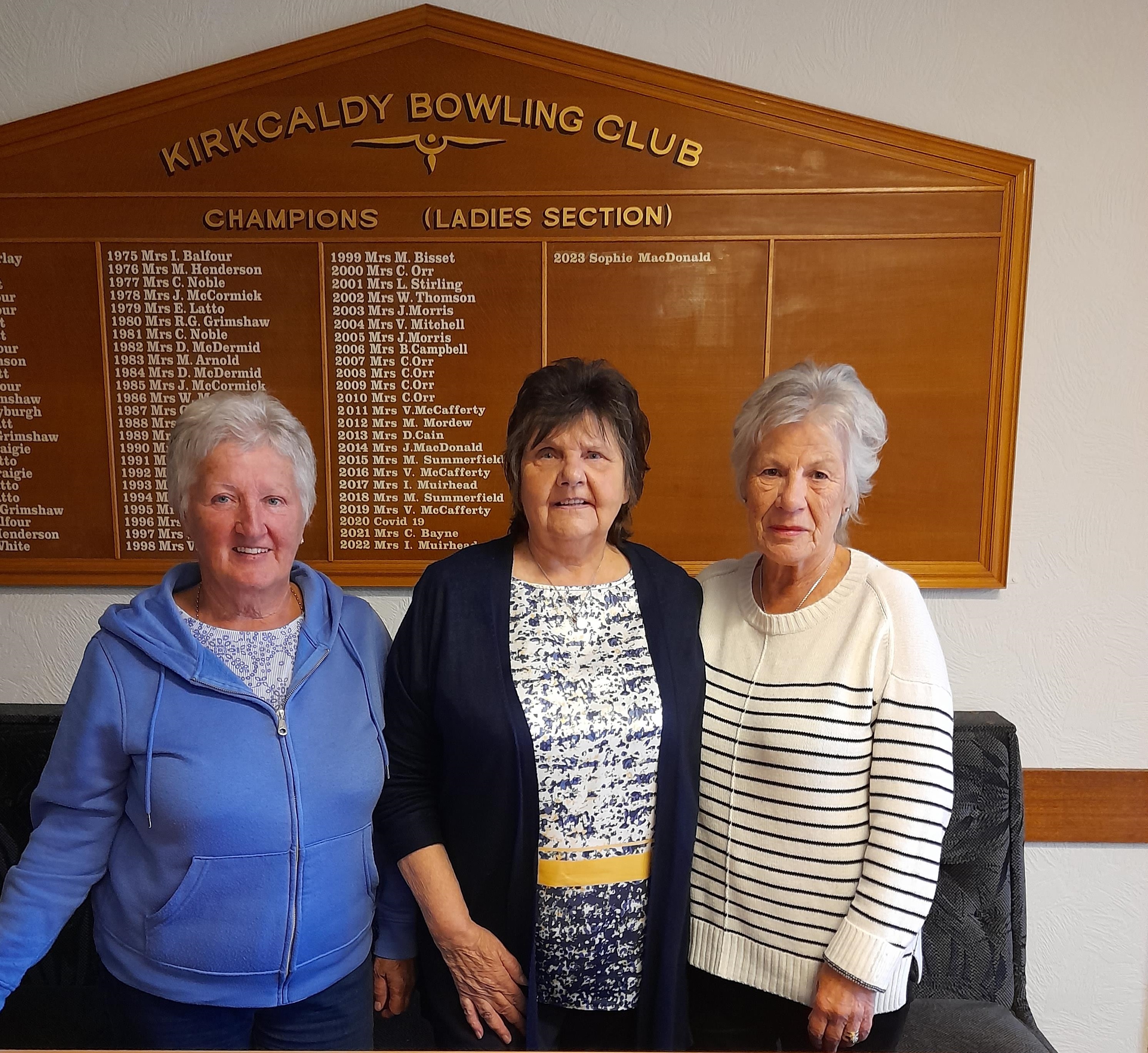 Three women standing in front of Kirkcaldy Bowling Clubs indoor sign.
