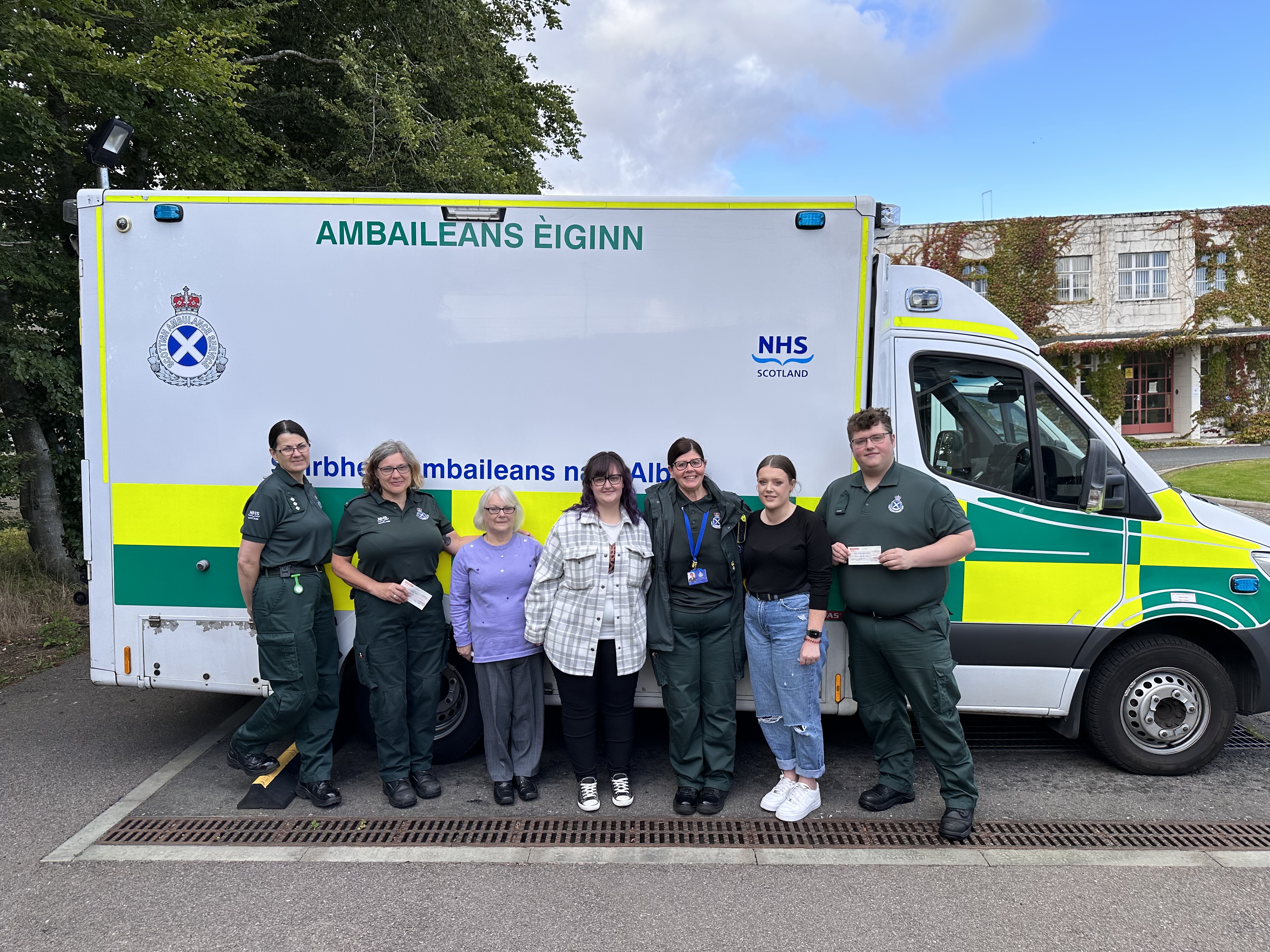 Scottish Ambulance Service staff with family presenting cheque in front of an ambulance