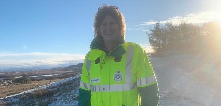 Skye volunteer Bridget Little dressed in high vis jacket standing on a snow covered road.