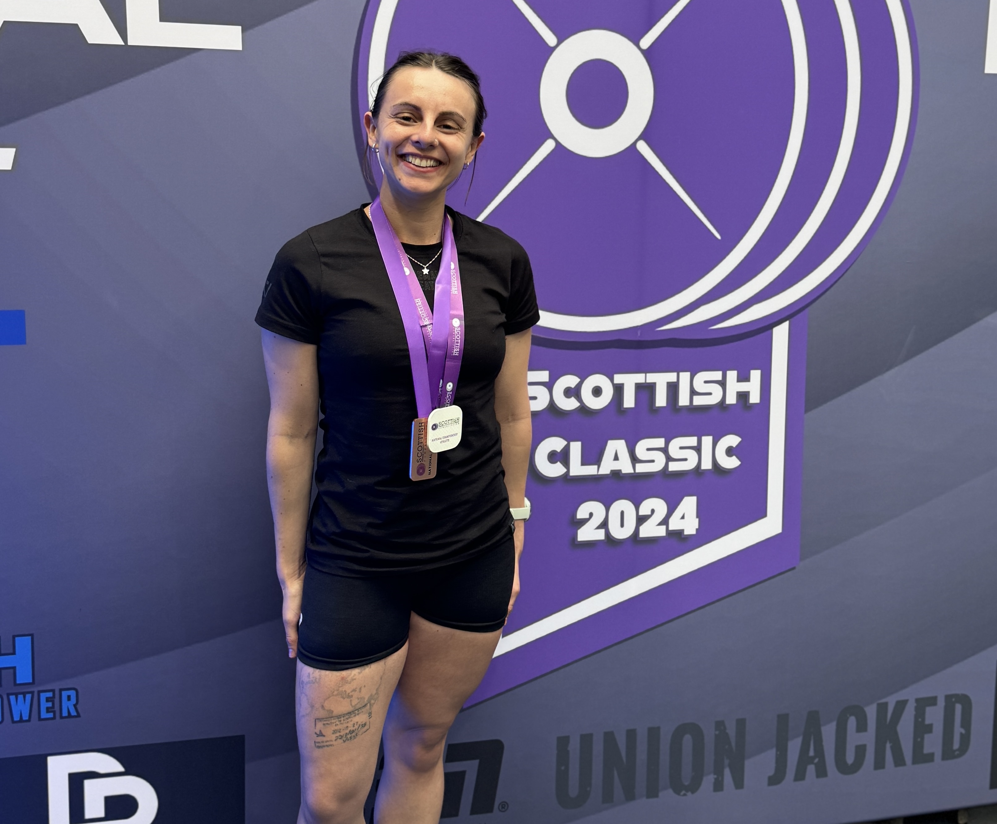 Kayleigh with a medal around her neck stands next to a board advertising Scottish Classic 2024