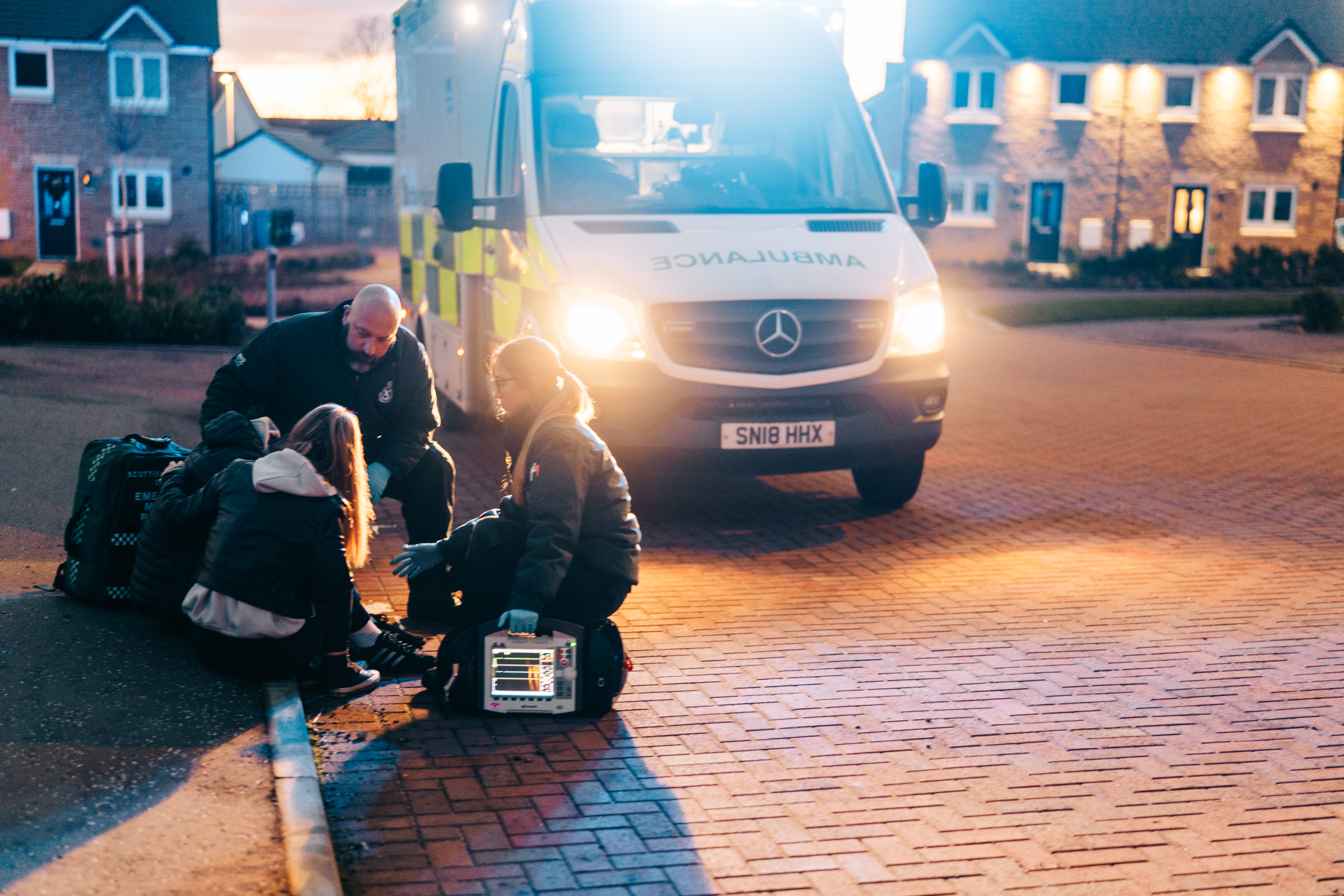 A crew treat a patient at the side of the road with the ambulance behind