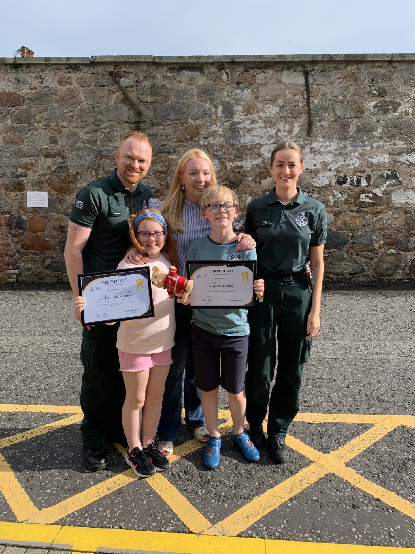 Siblings presented with their certificates by the Scottish Ambulance Service stand next to SAS staff members