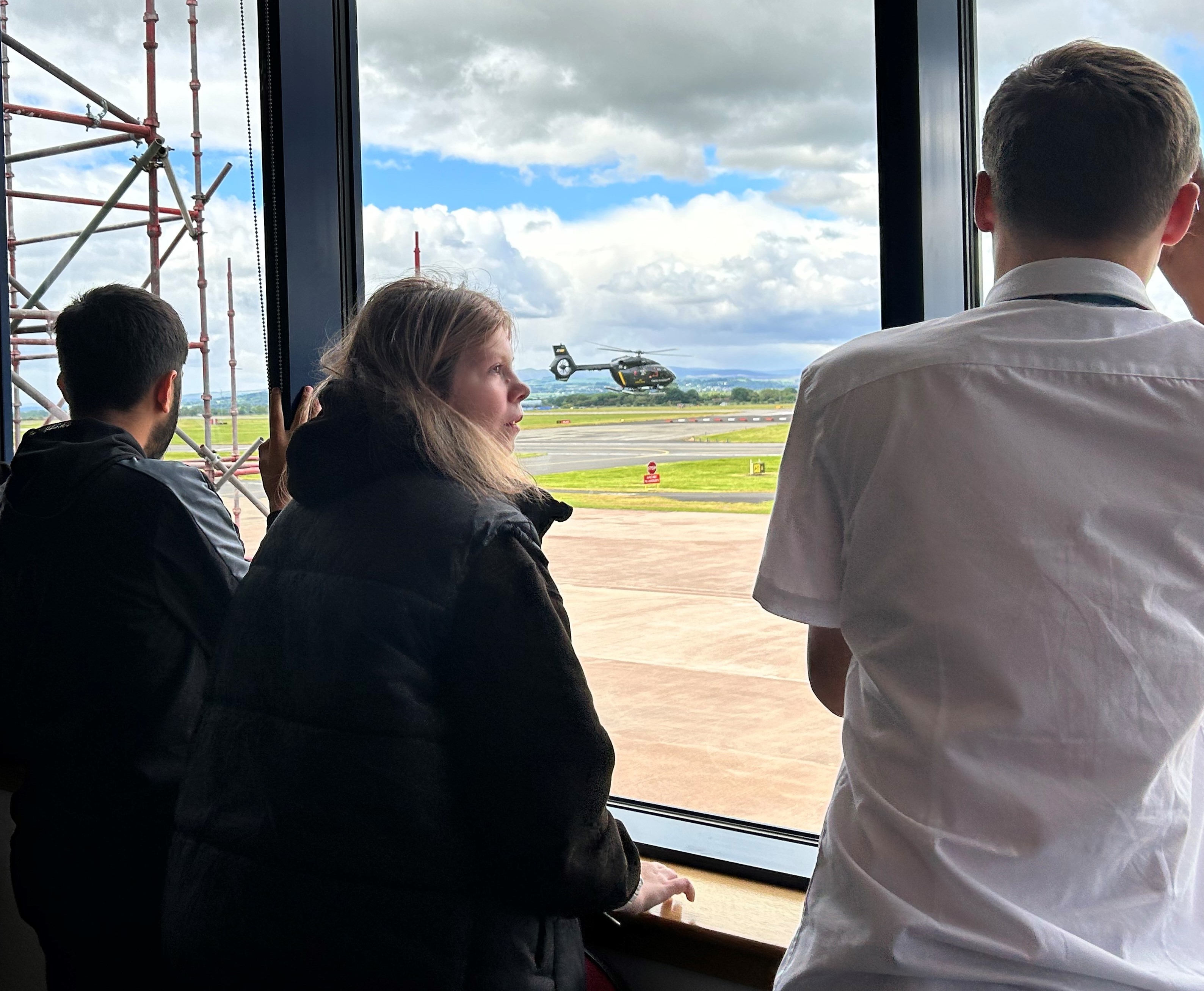 Three school pupils watching an air ambulance land from an inside window.