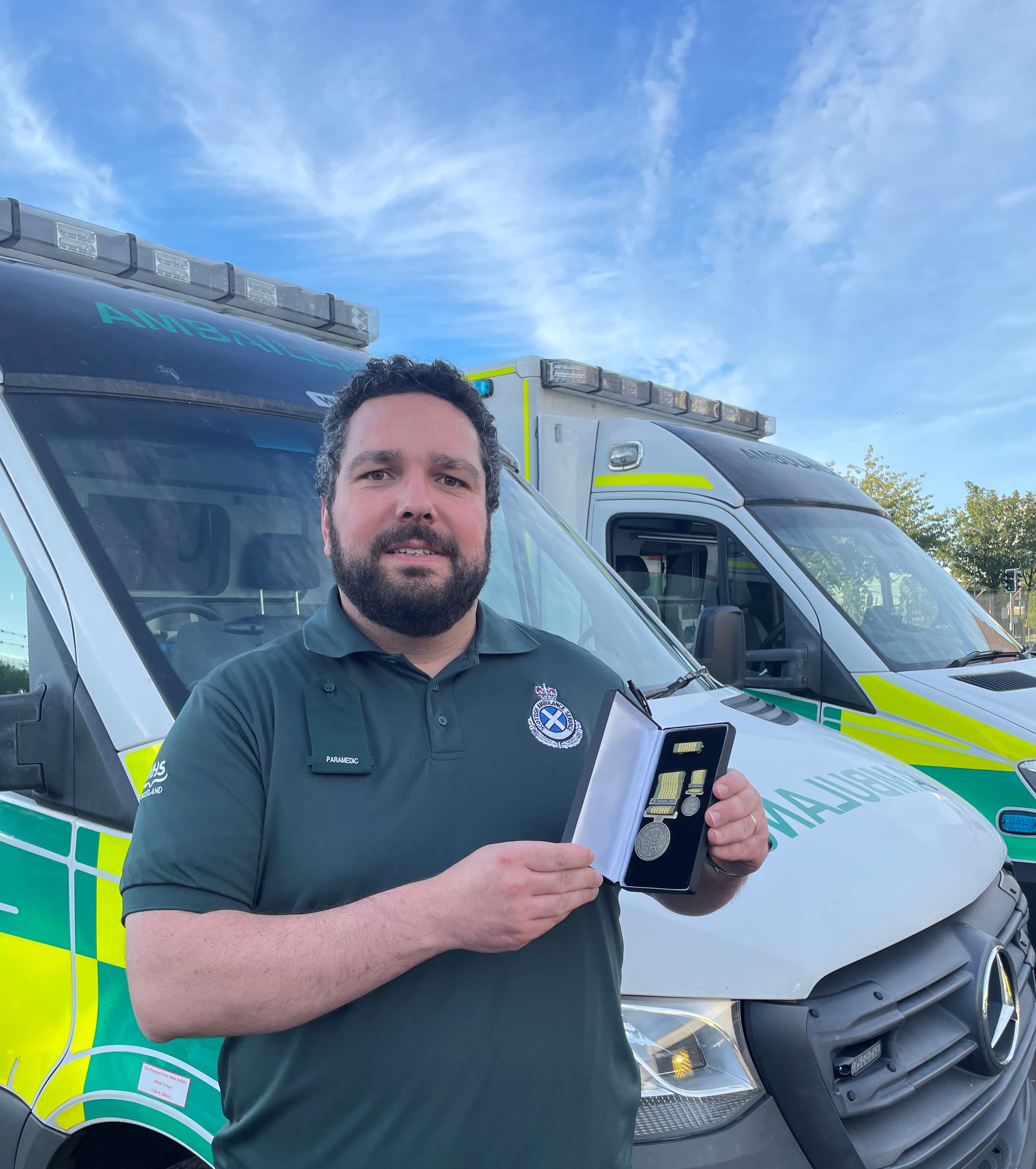 Paramedic Steve holding his medal in front of an ambulance