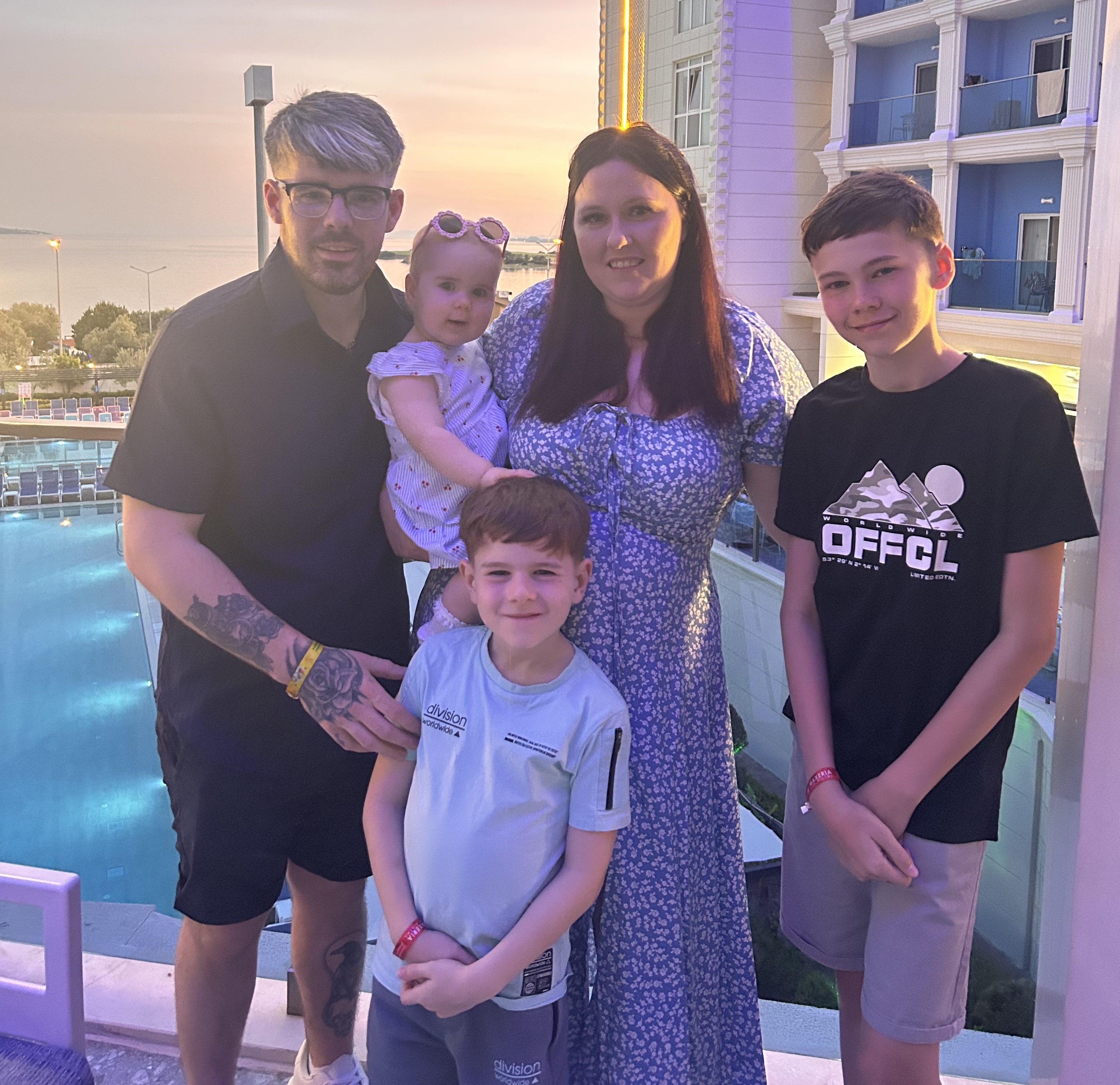 Shannon and her entire family pose for a photo on a holiday. Kids and husband look towards camera with the sun setting in the background