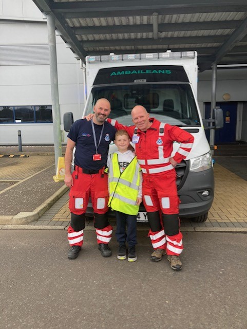 SAS staff members dr Davis and Steven McIntosh smile with Calon in the centre, with an ambulance vehicle in the background