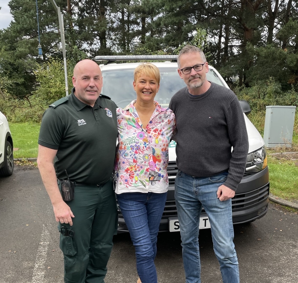 Patient Suzie celebrates her reunion with Andy and her husband with an ambulance in the background