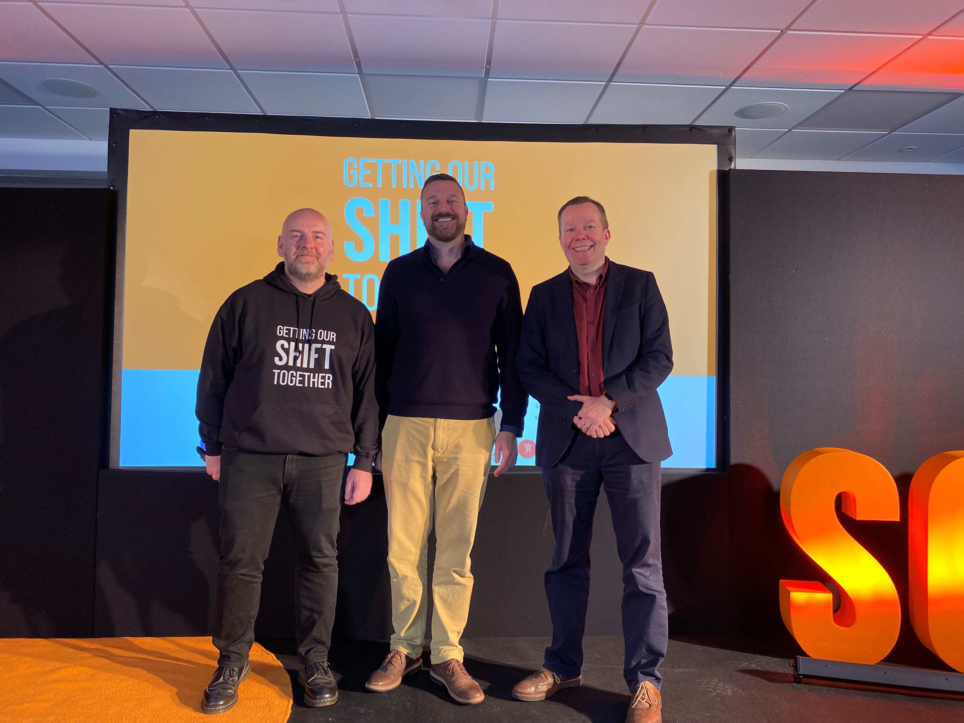Three men stood on the stage smile at the camera at the Scottish Cardiac Arrest Symposium 2023