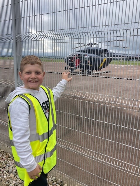 Calon, with a big smile on his face, looks out through a fence at a helicopter