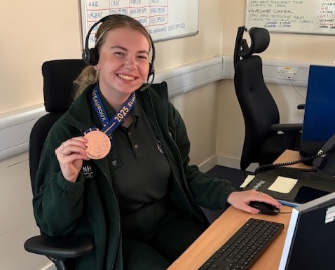 Izzy proudly displays her bronze medal at her computer screen