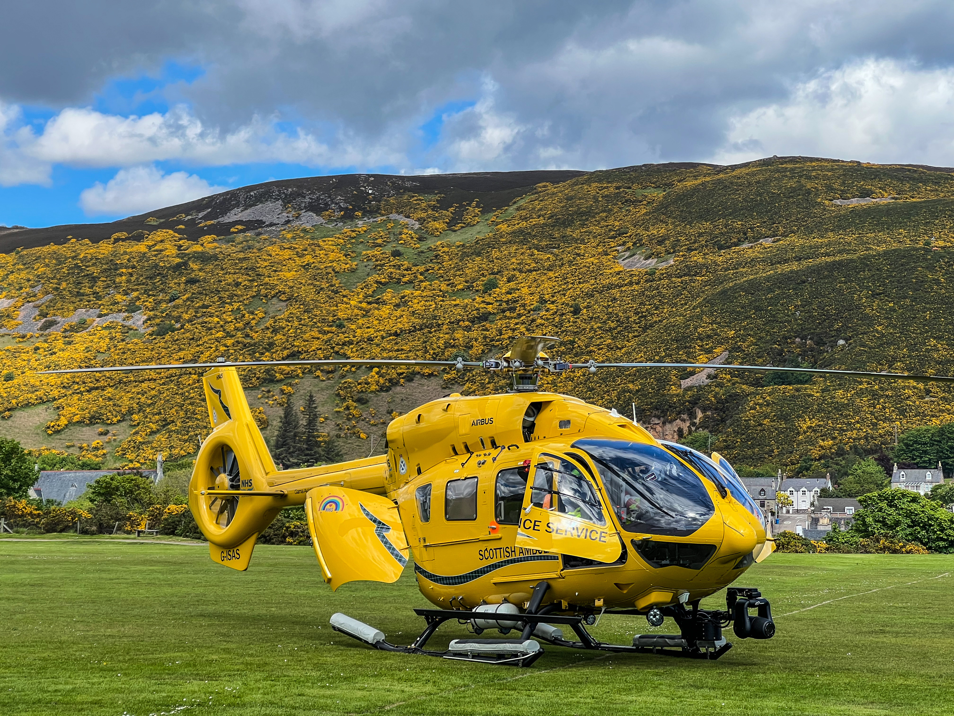 A Scottish Ambulance service helicopter in a field with a hill in the backlground