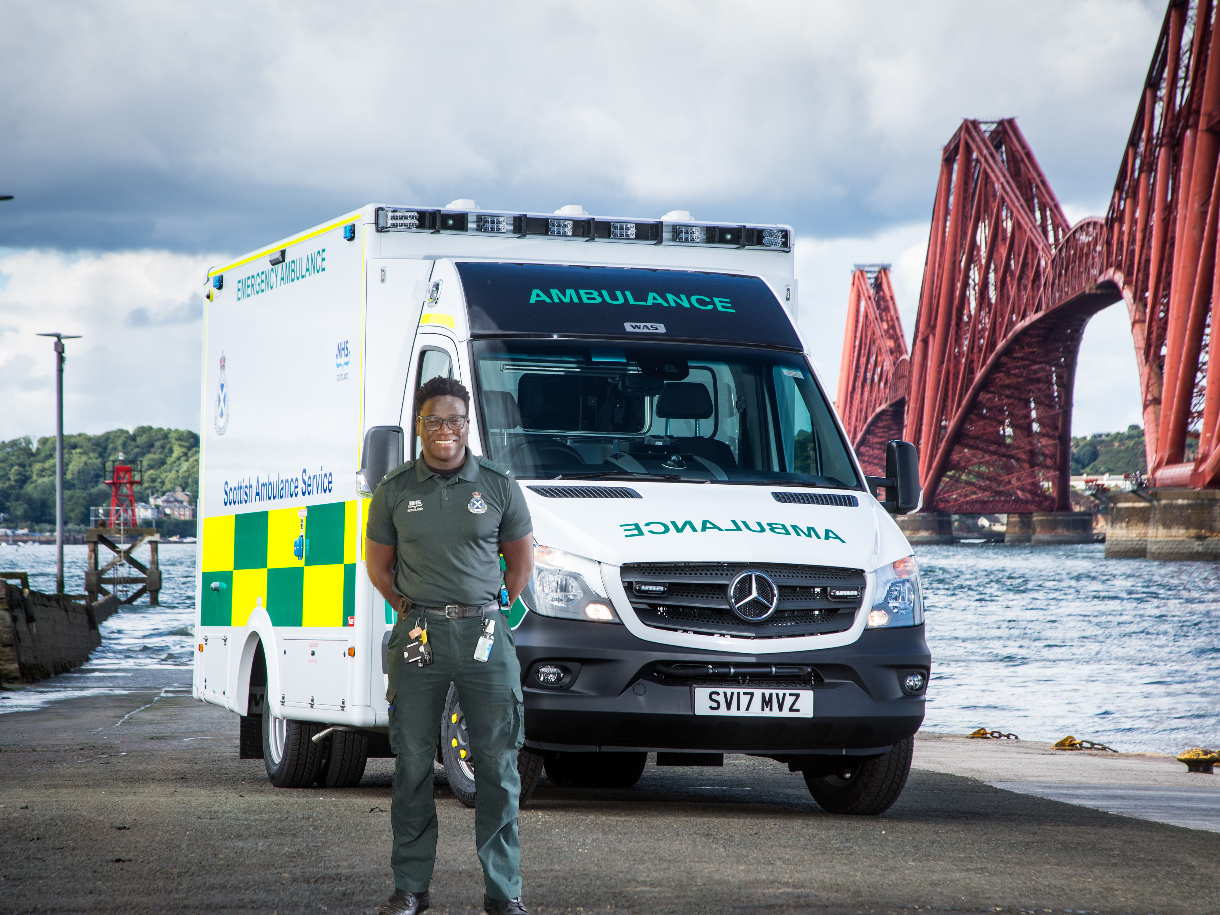 An Ambulance Technician standing in front of an A&E ambulance with the Forth Bridge in the background