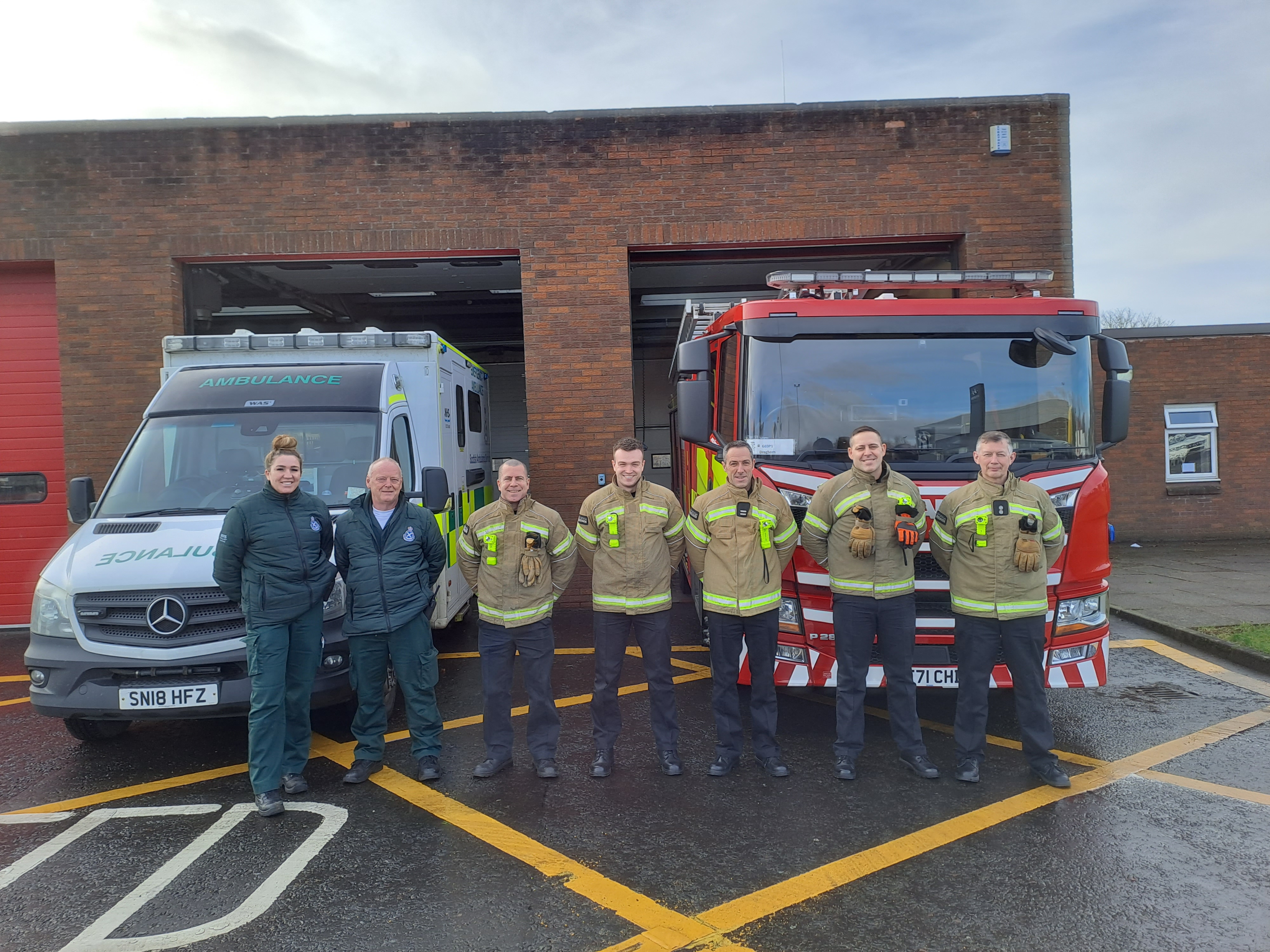 Ambulance staff with Scottish Fire and Rescue staff stand in front of an ambulance and Fire Engine at a station