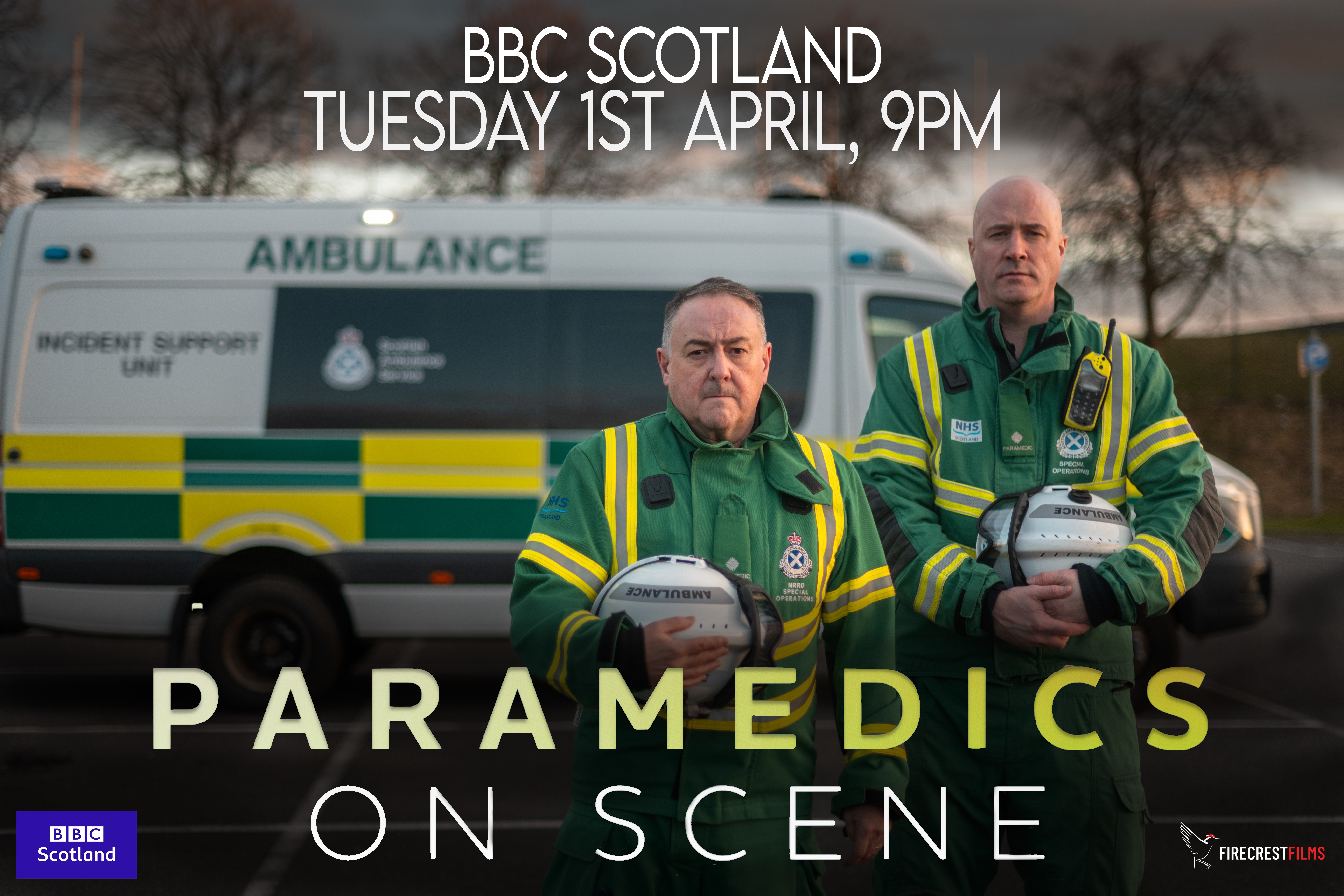 Two SORT members of staff stand proudly with their helmets with the title card of the show highlighted in front