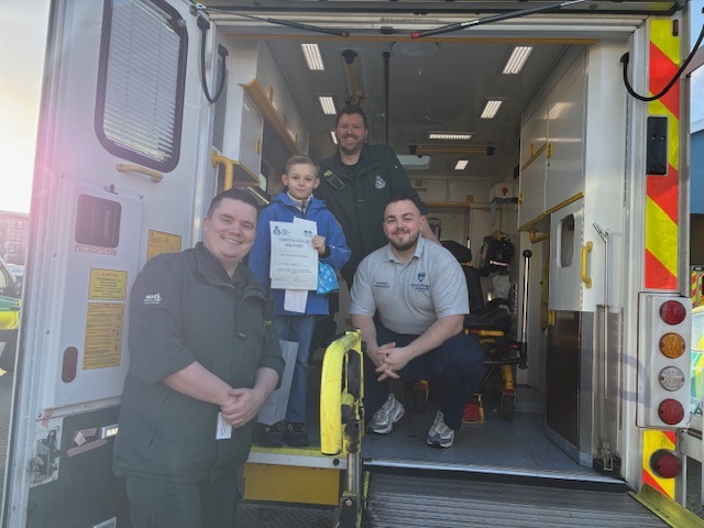 Christopher holds his certificate in the back of an ambulance with the SAS staff who treated his dad