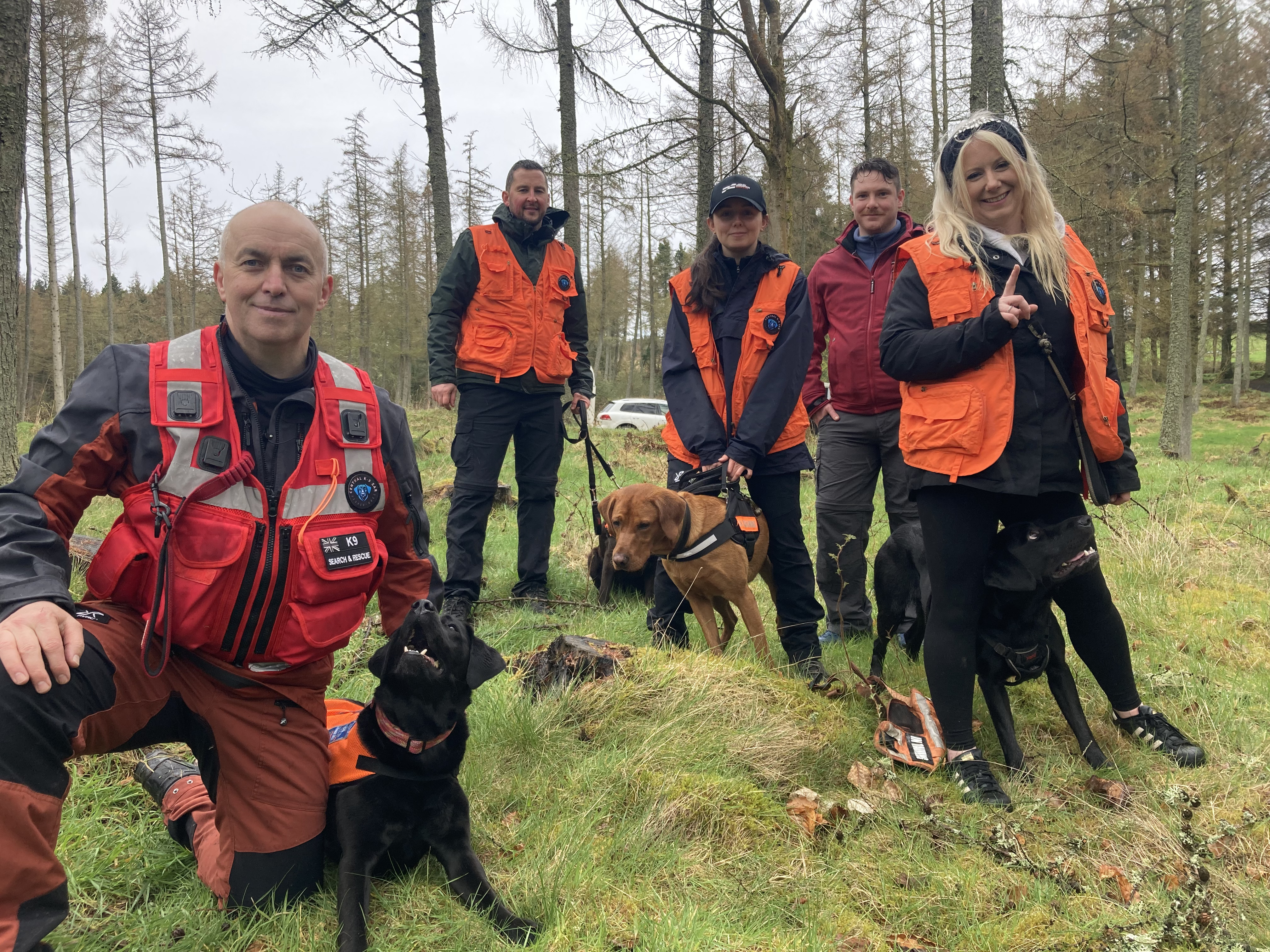 Steve, the dog leader, poses with his dog Poppy and the other dog handlers in the background smiling with their dogs
