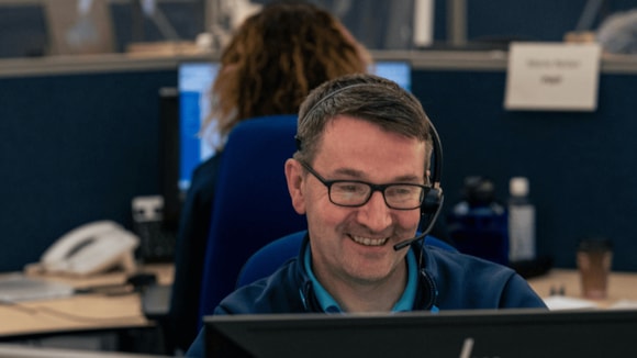 Smiling NHS 24 call handler sat at a desk with a headset on.