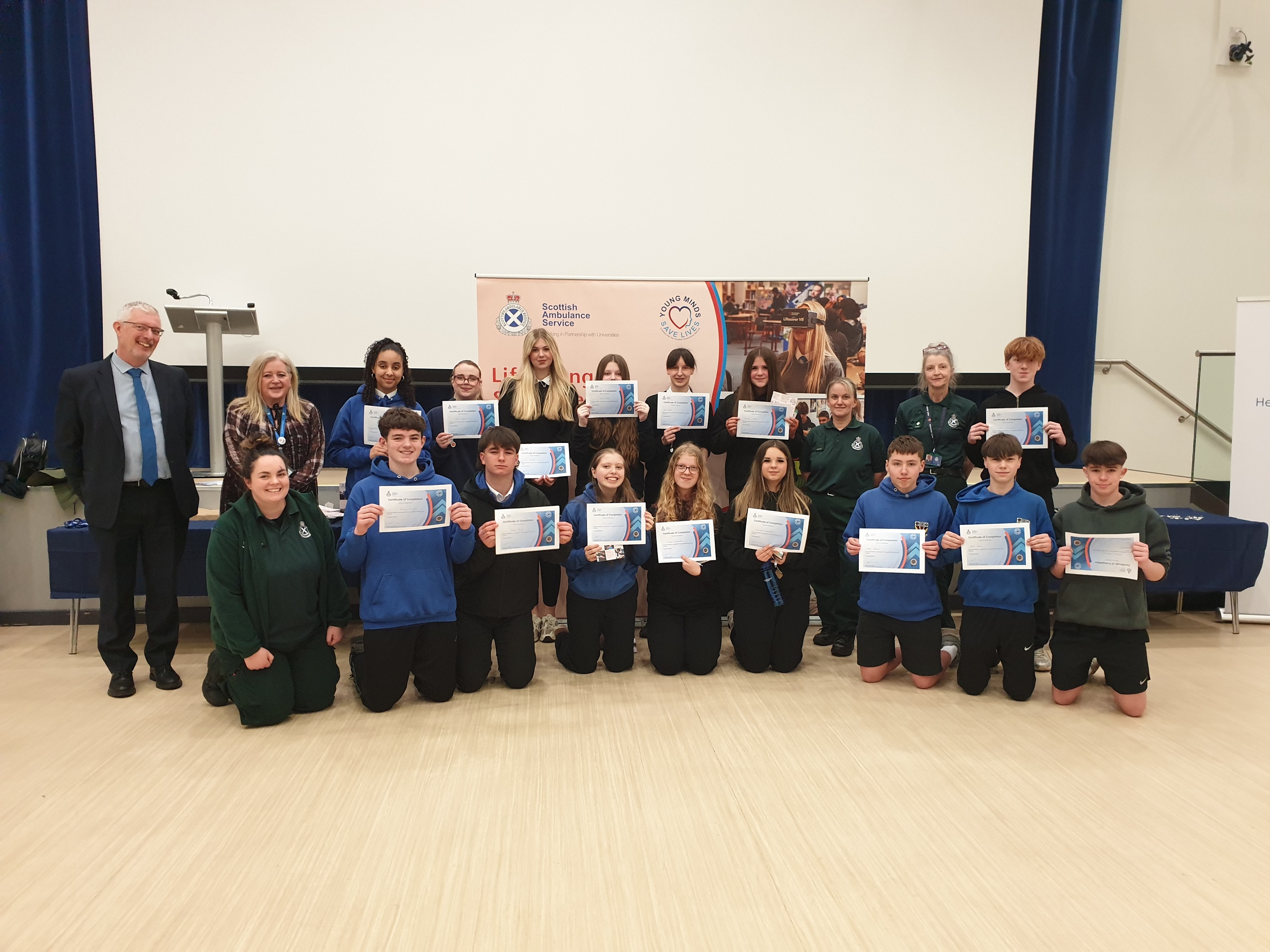 Group of students and teachers posing indoors, each student holding a certificate of achievement.