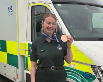Izzy proudly displays her medal standing in front of an ambulance vehicle