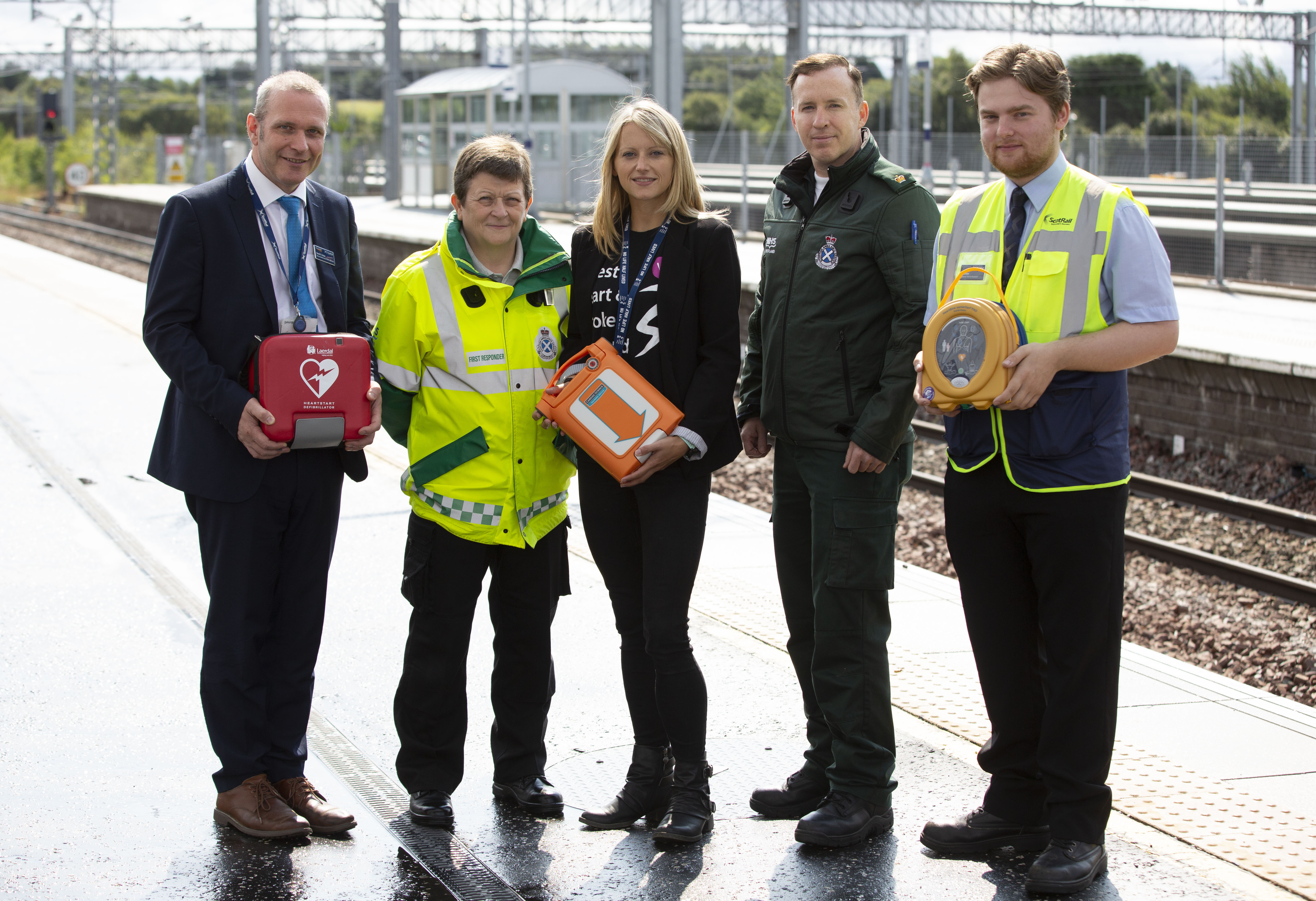 Five people with a public access defibrillator on a railway platform