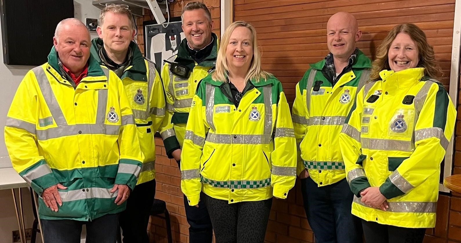 Penicuik Community First Responder Group - 4 men and 2 women are dressed in high vis community first responder jackets stood together and smiling at the camera.