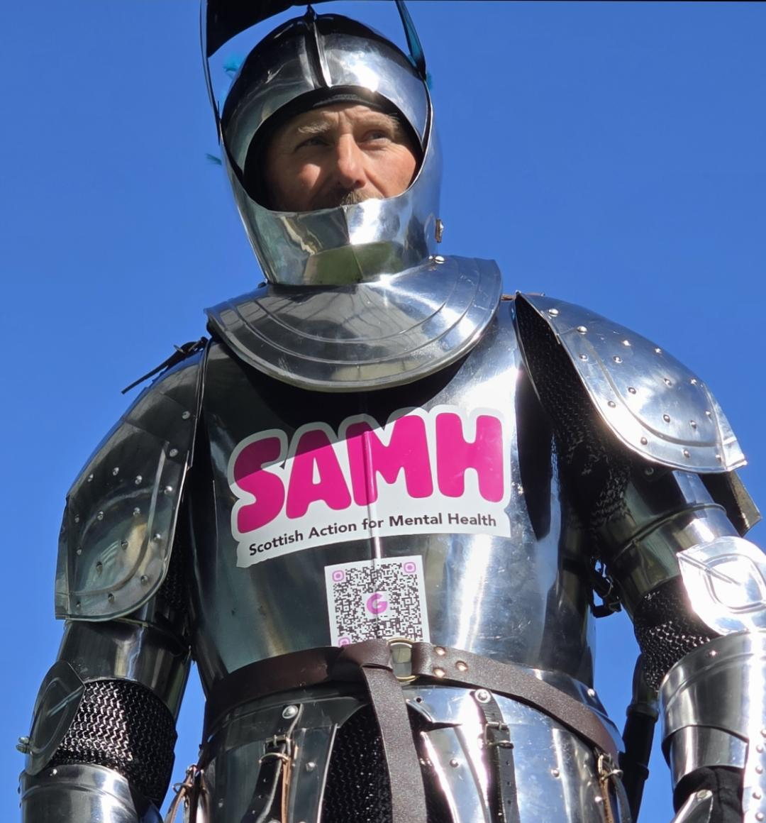 Jay Watt dressed in a full suit of armour with the SAMH logo on the chest.