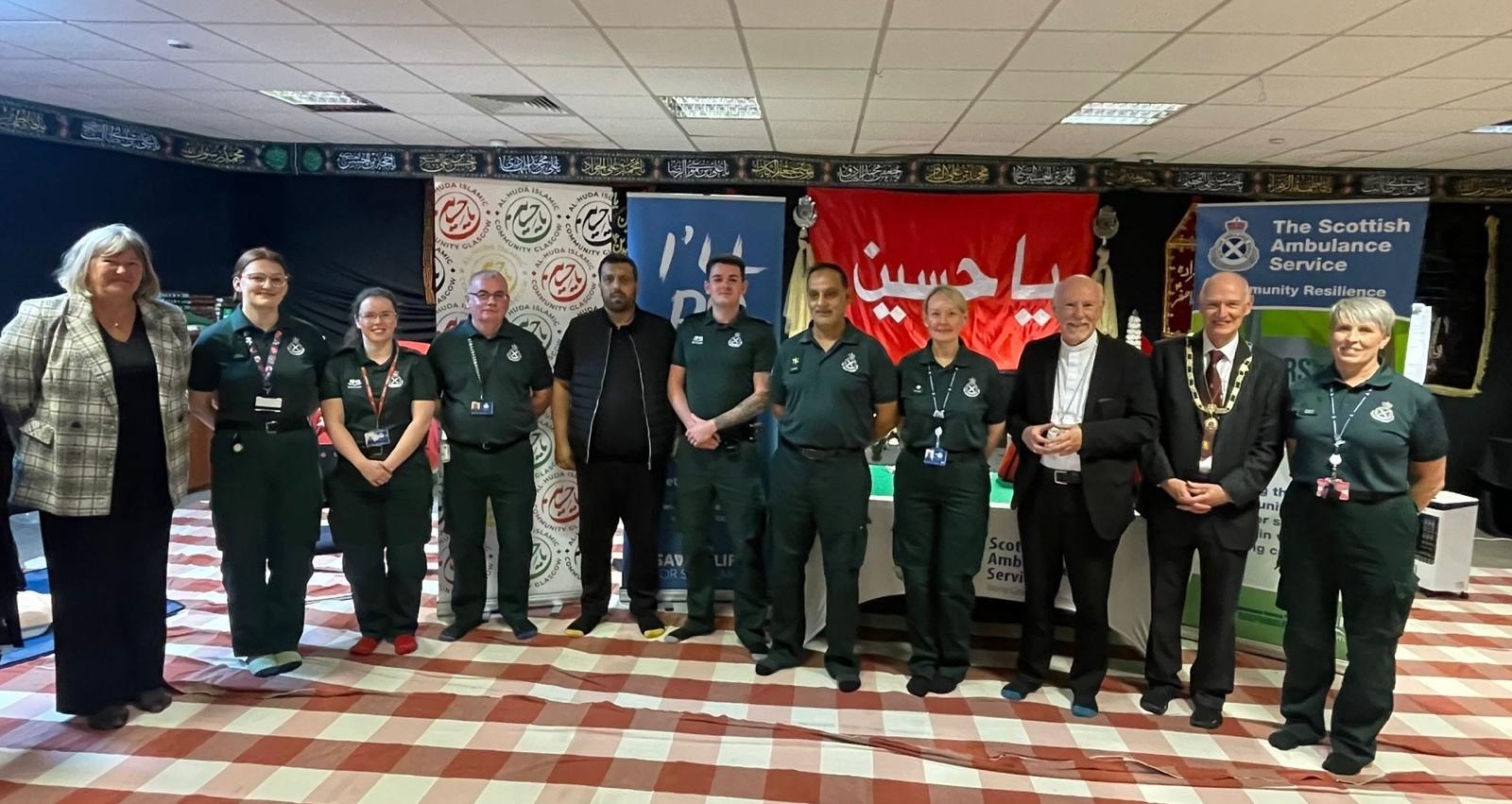 Scottish Ambulance staff and members of the public stand in front of advertising boards
