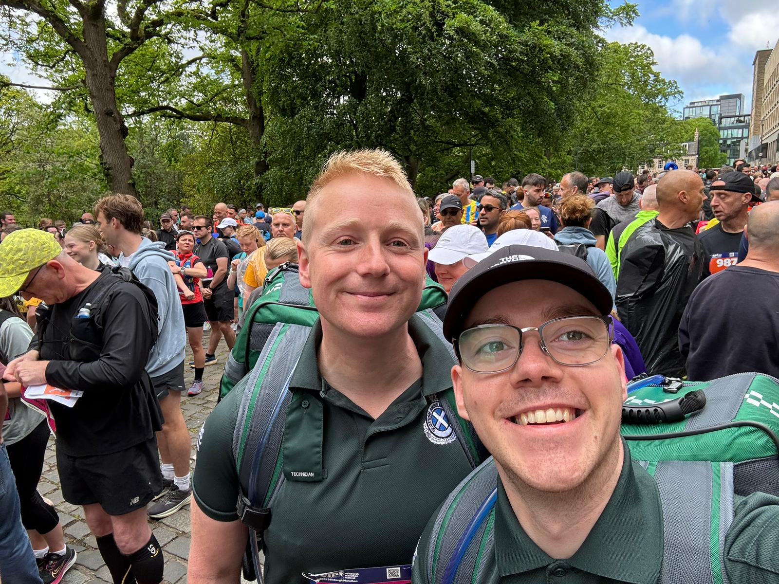 Jack and Dominic take a smiling selfie at the marathon with crowds behind them