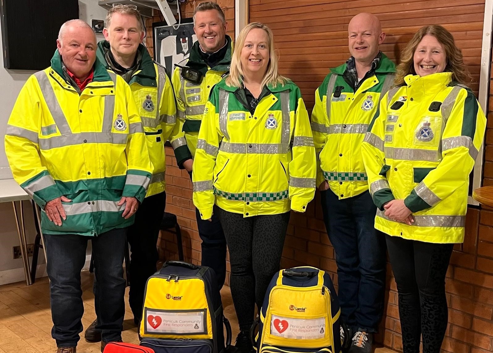 Penicuik Community First Responder Group - 4 men and 2 women are dressed in high vis community first responder jackets stood together and smiling at the camera.