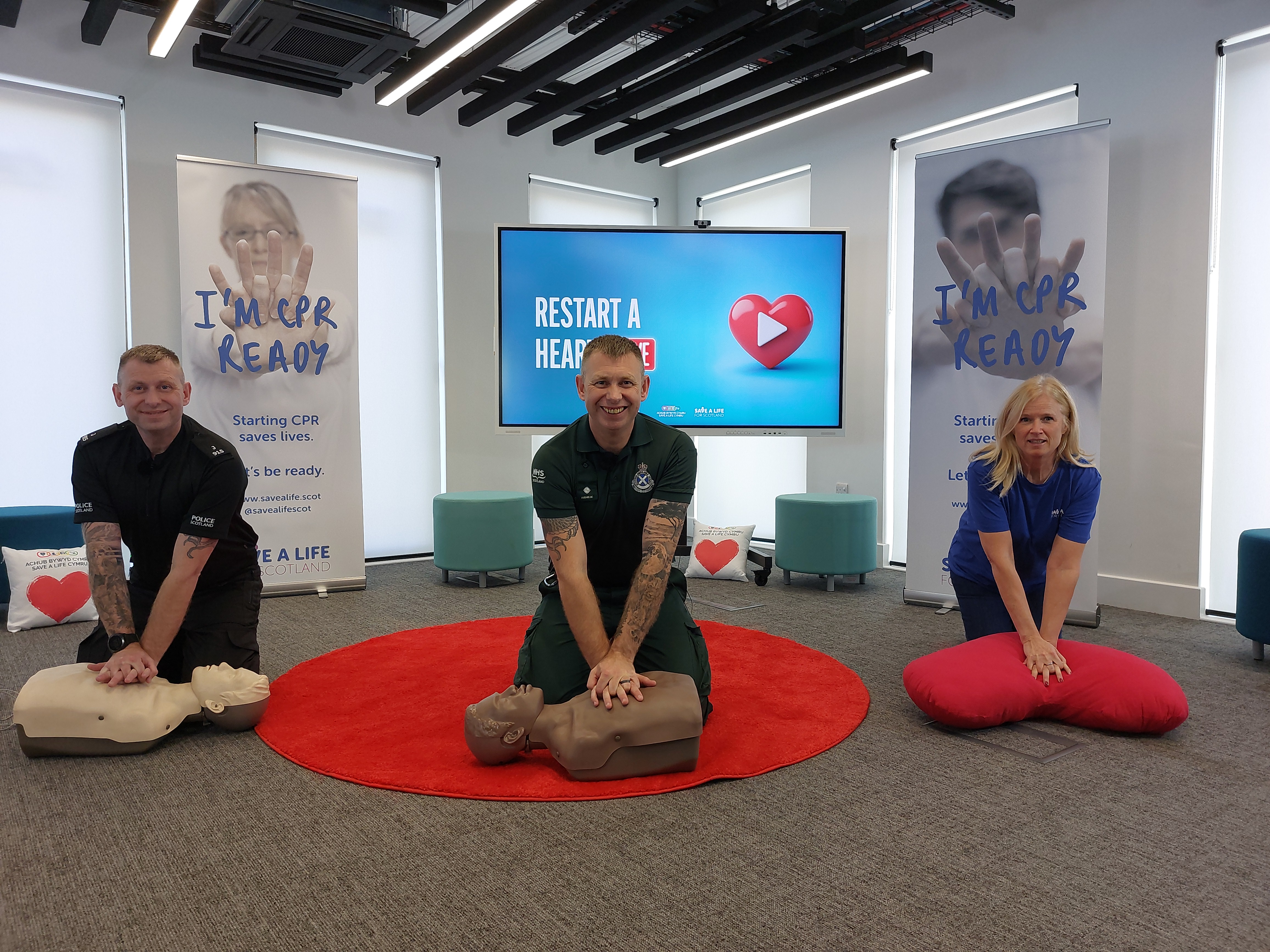 Liam Myers, Lee Myers and Susan Gardner performing CPR on dummies and a heart shaped pillow.