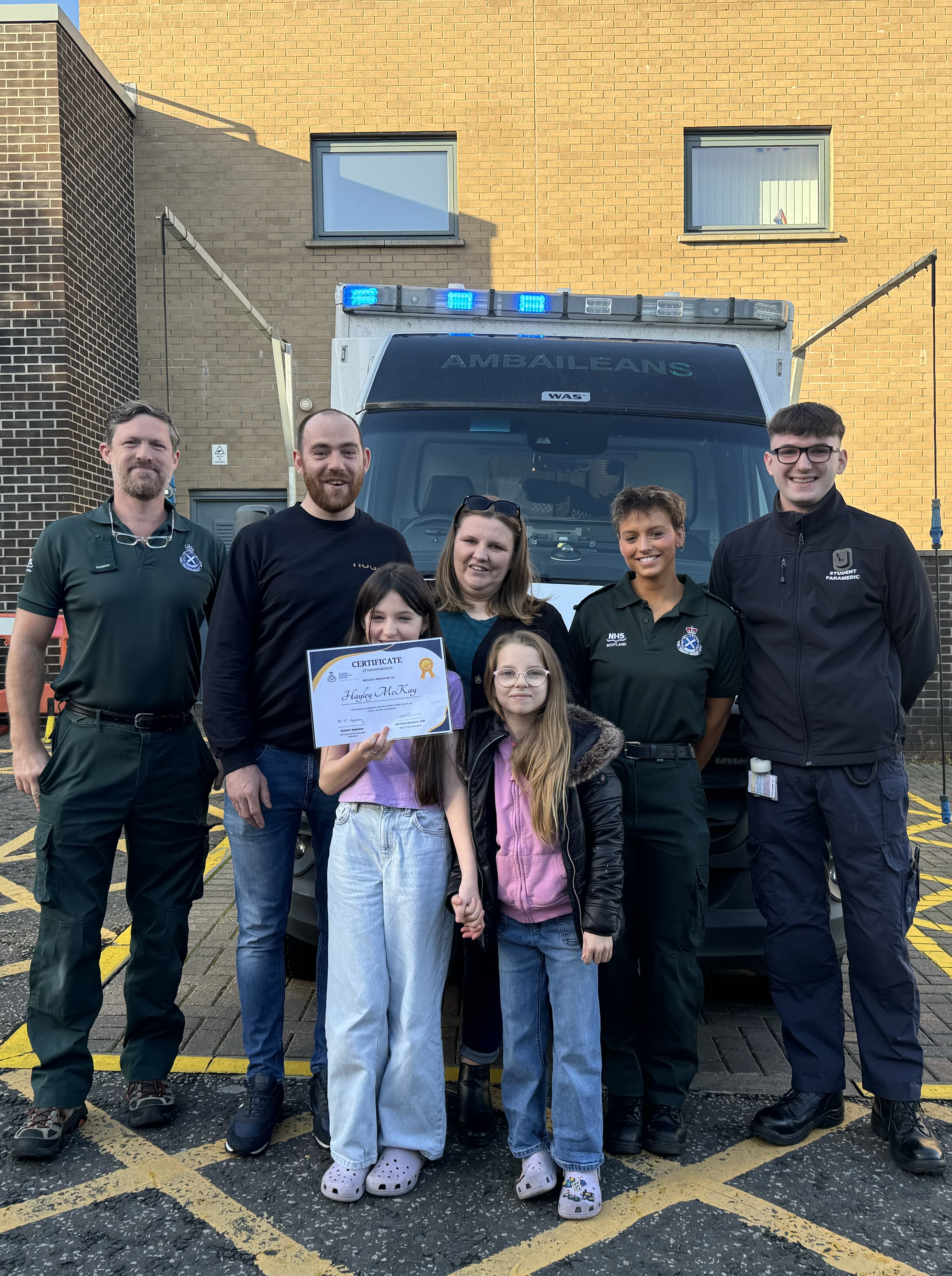 Hayley holds her certificate proud with her sister dad and Scottish Ambulance Service staff who helped