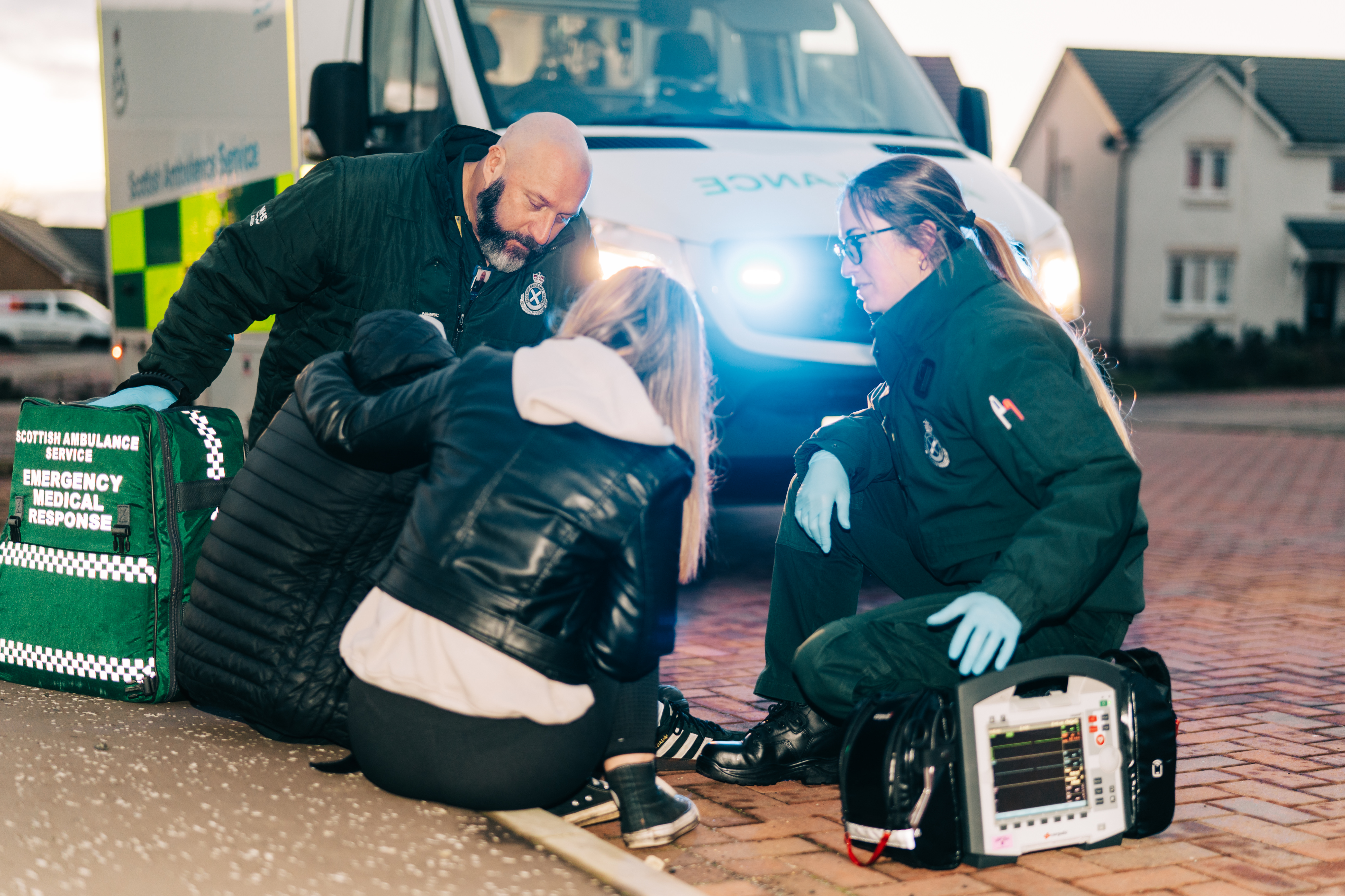A crew treat a patient at the side of the road with the ambulance behind