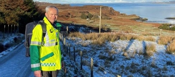 Skye volunteer Steve Brealey dressed in high vis jacket standing on a snow covered road.