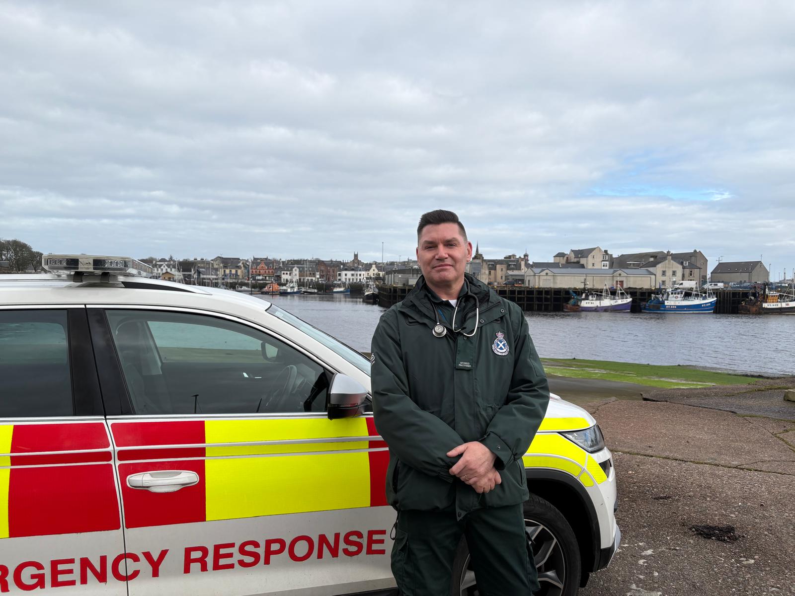SAS Ambulance worker in uniform stood by a parked ambulance vehicle