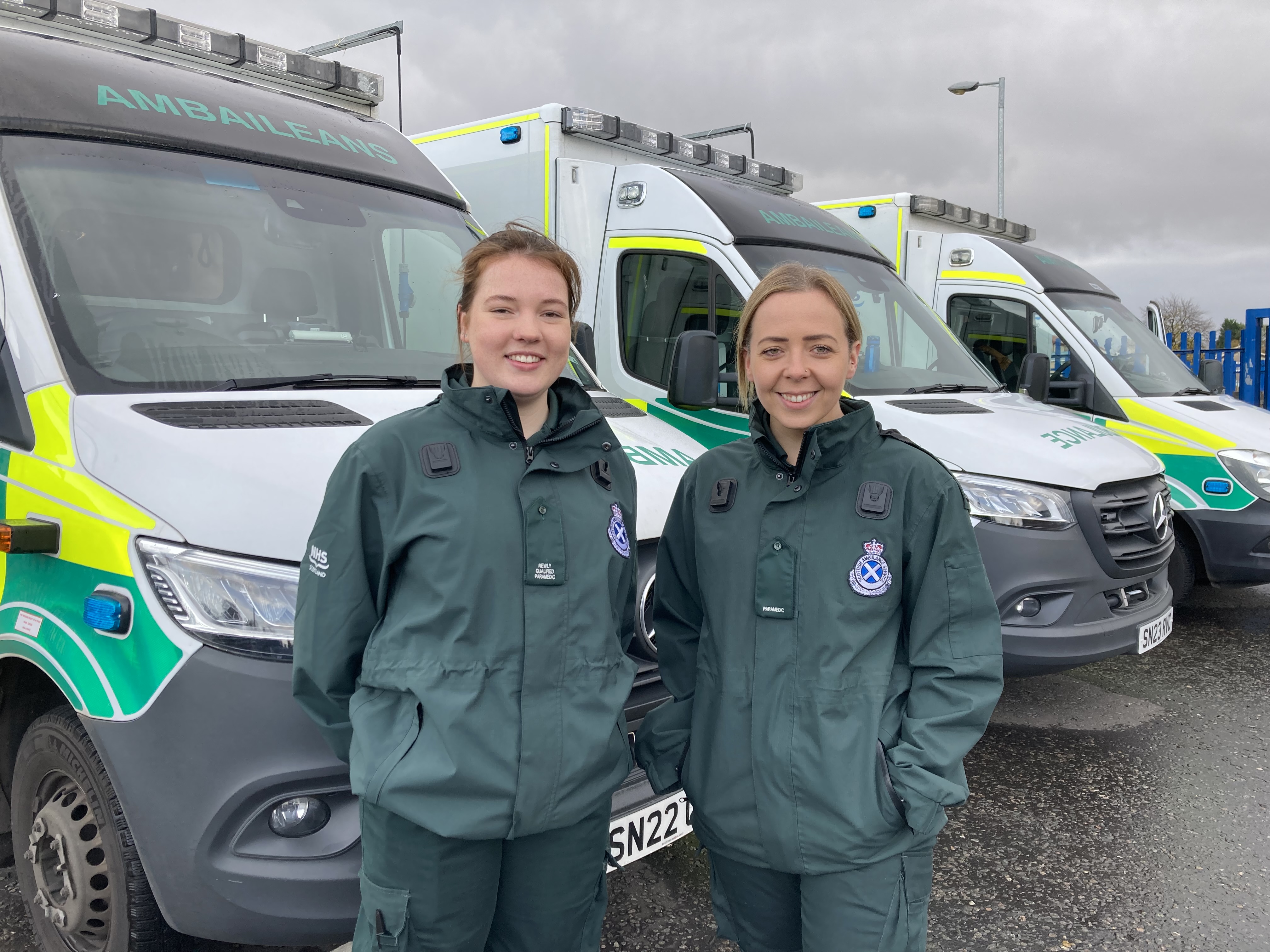 Two female members of ambulance staff stand in front of some ambulances