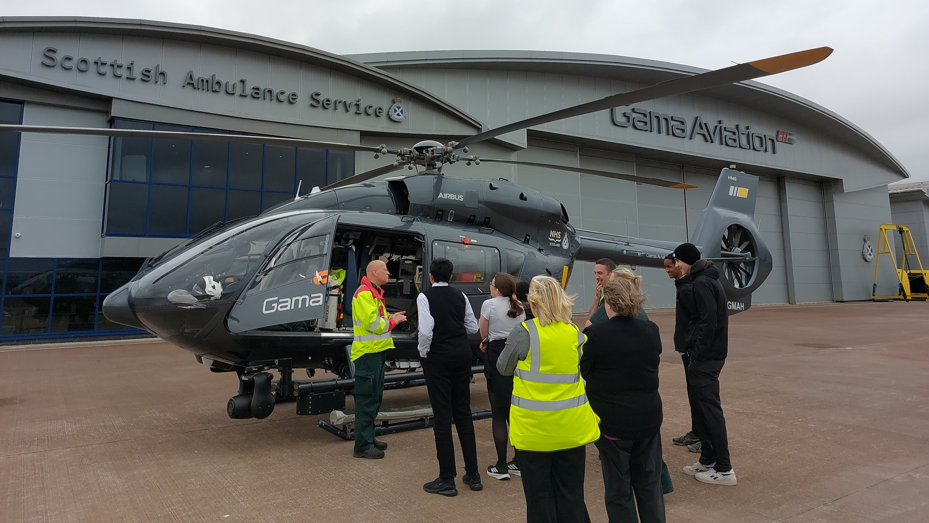 A group of school children listening to ScotStar paramedic who is giving a tour of a grey air ambulance.