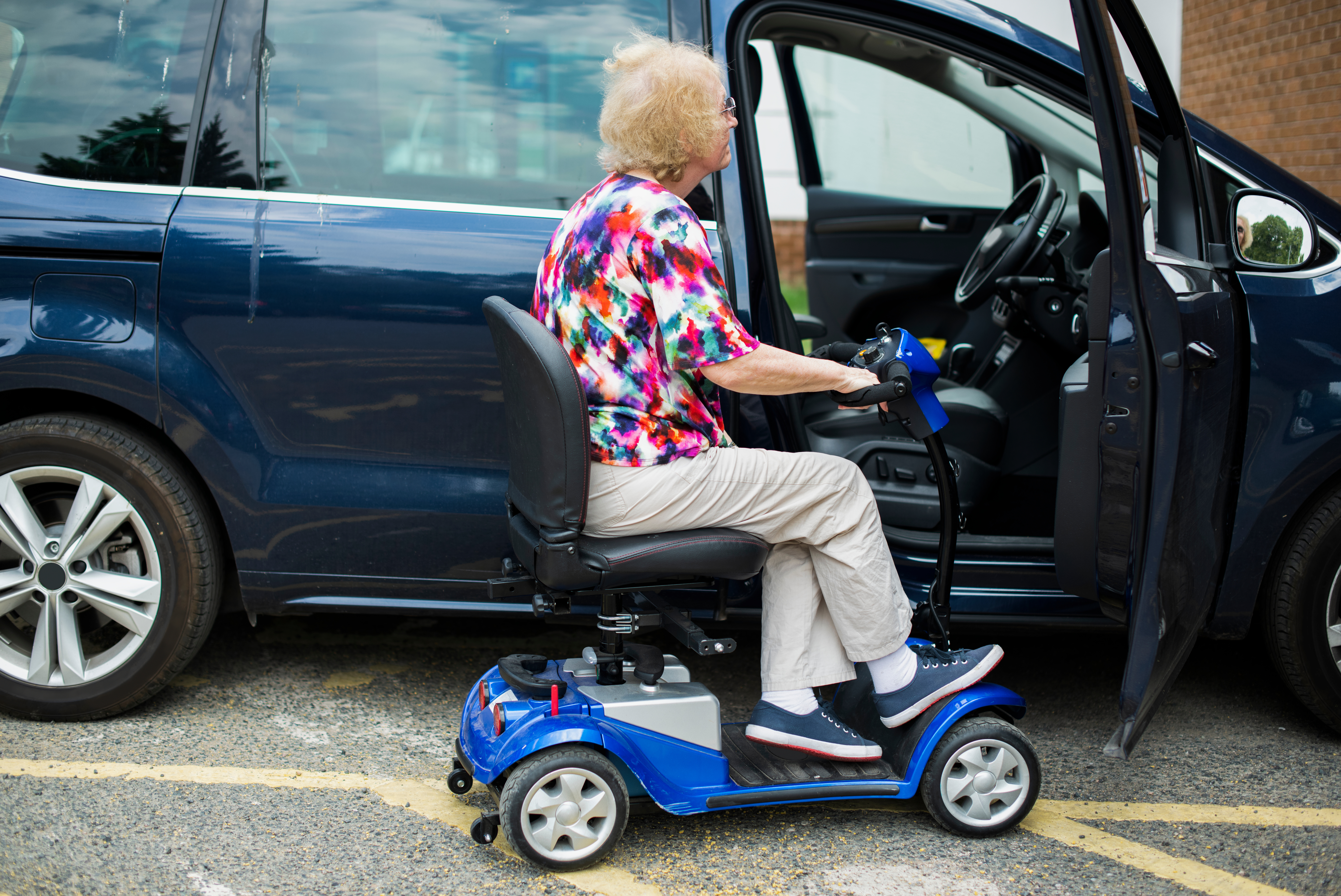 A lady in a mobility scooter about to get into a car