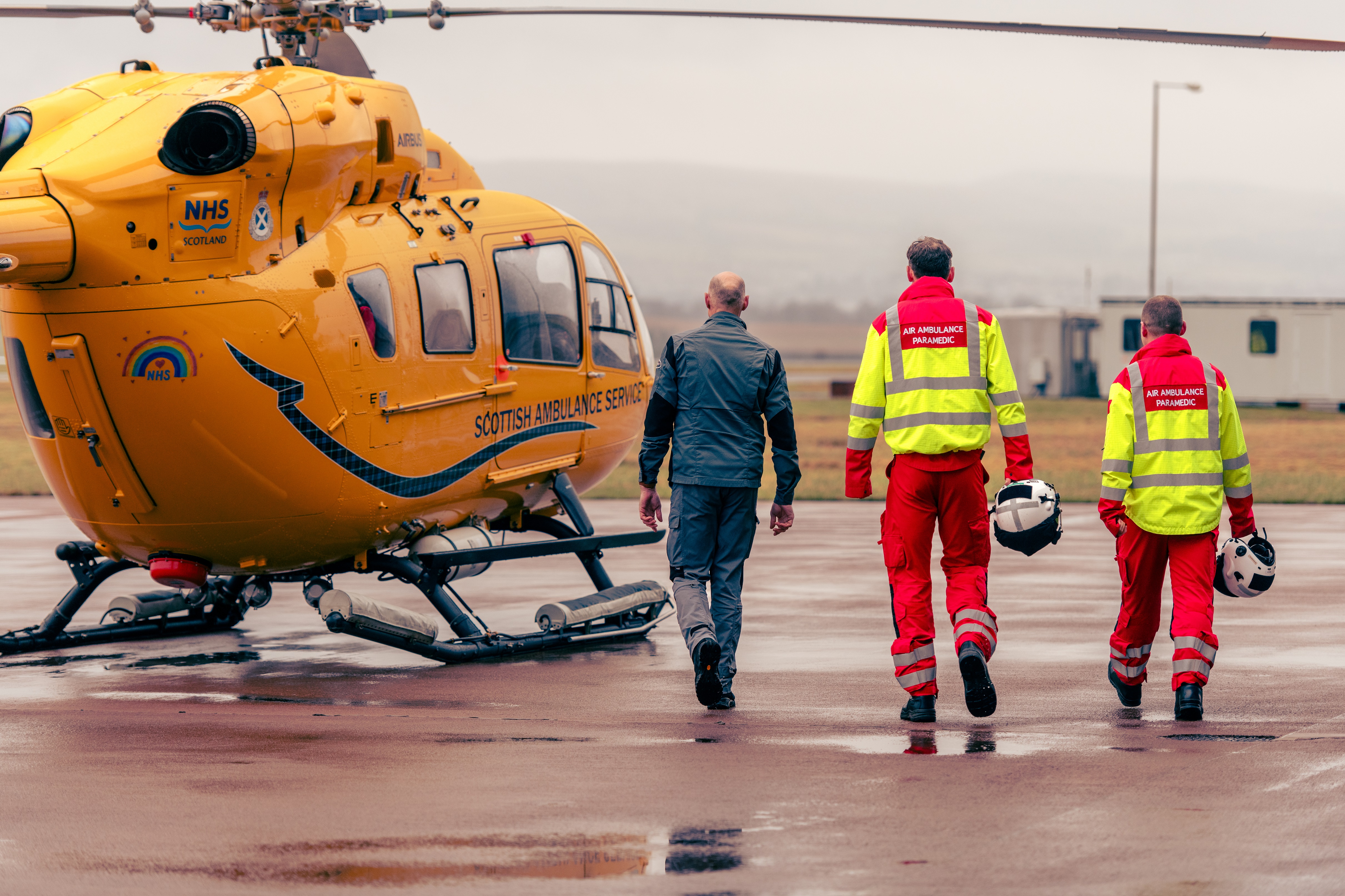 Three members of a helicopter crew walk towards the helicopter on the tarmac